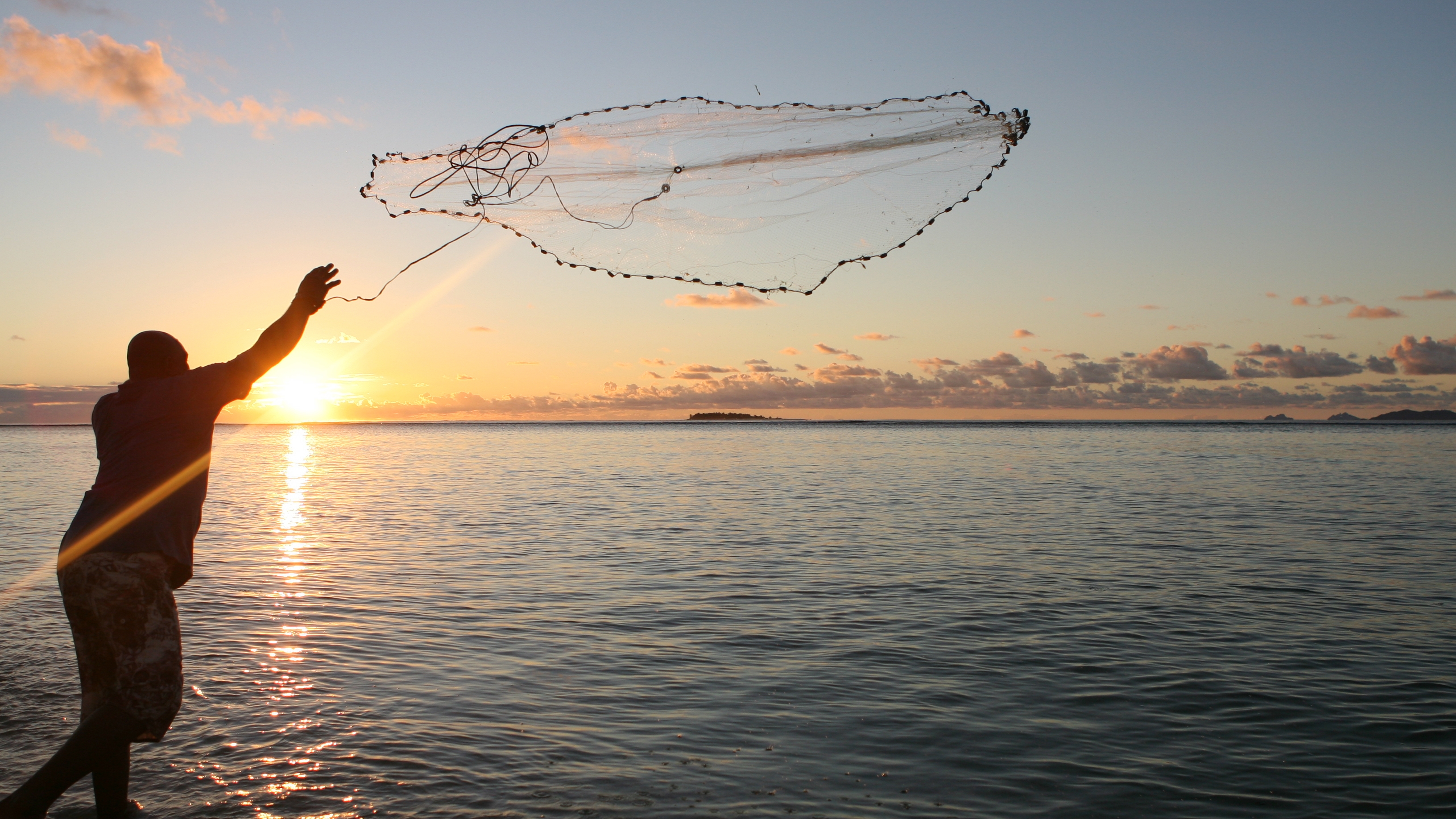 A man throws a fishing net during sunset in Fiji